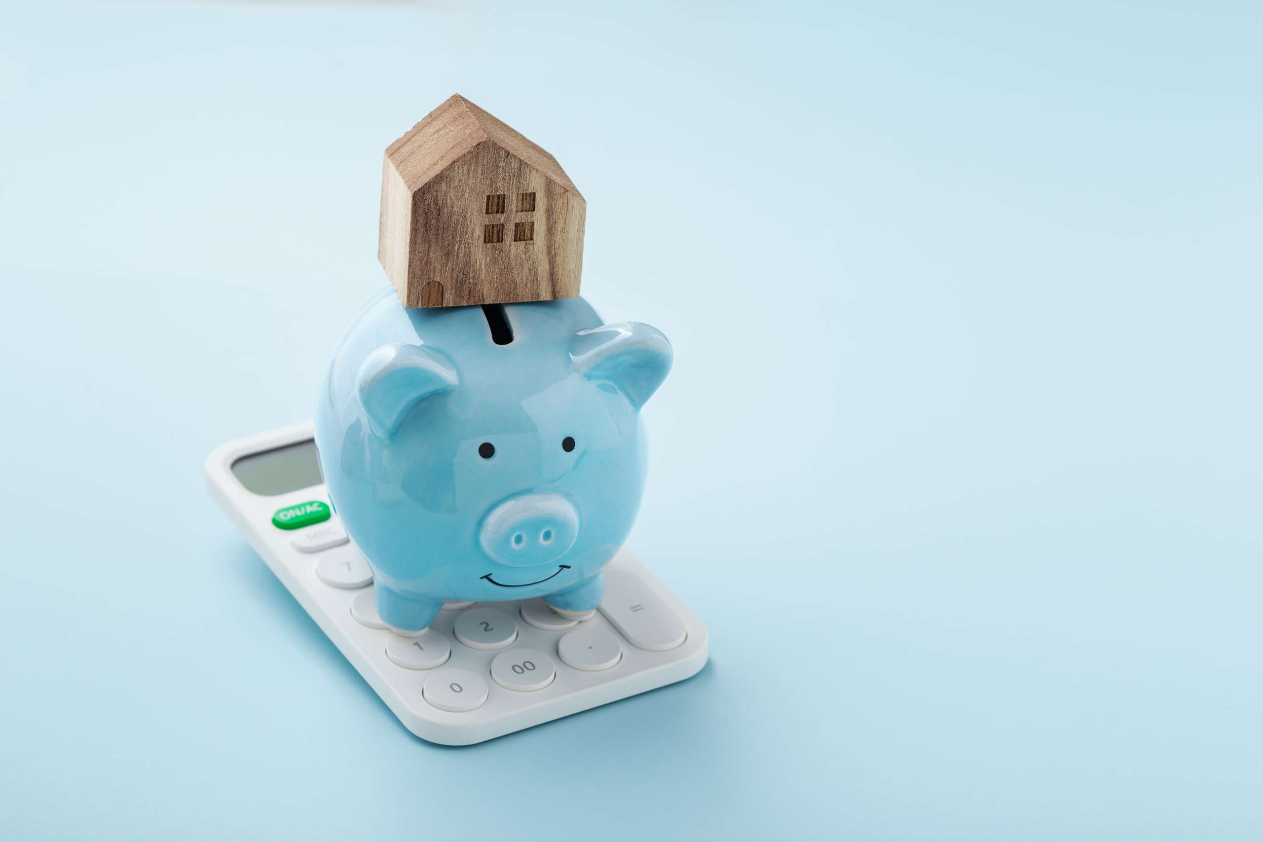 House on piggy bank and calculator on blue background with copy space